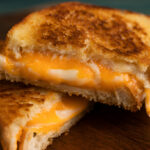 A golden, crispy grilled cheese sandwich with gooey melted cheese inside, served on a rustic wooden plate.