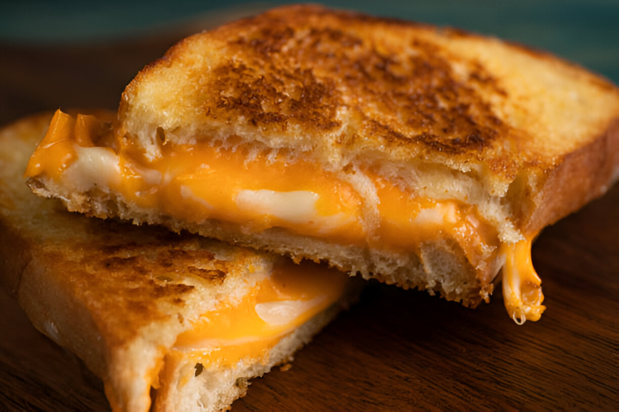 A golden, crispy grilled cheese sandwich with gooey melted cheese inside, served on a rustic wooden plate.